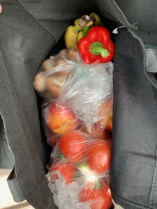 assorted fresh produce, some of it in clear plastic bags, inside a reusable bag